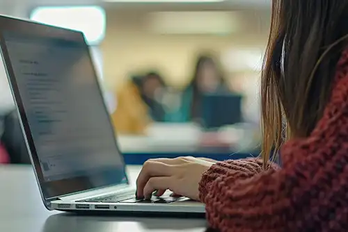 Studentessa digita su un laptop in un'aula affollata